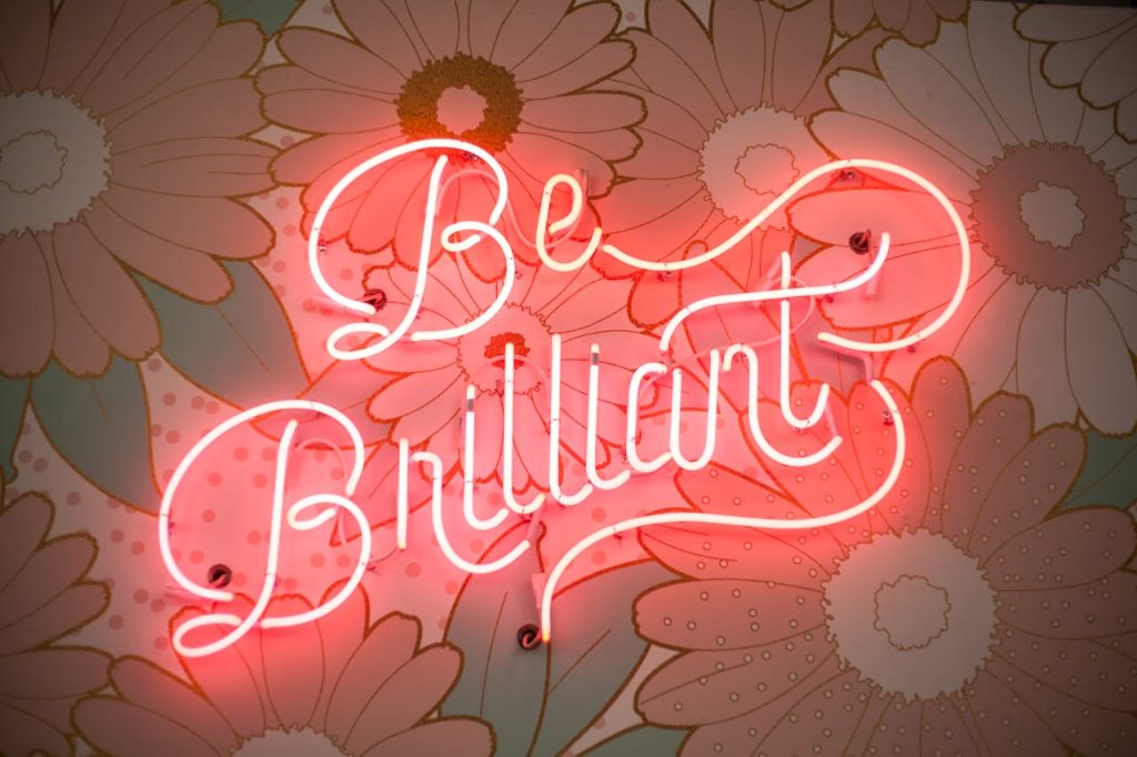be-brilliant-neon-light-2002719 A glowing neon sign reading Be Brilliant against a floral backdrop creates a vibrant and motivational atmosphere.